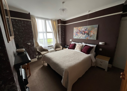 A Pendrin bedroom with deep plum walls, a double bed dressed in white linen and a tall window