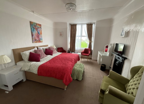 A light-filled Pendrin guest room with a large bed, armchairs and a window over the garden