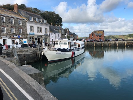 Slate-fronted Cornish harbourside buildings beside a moored passenger boat on still water